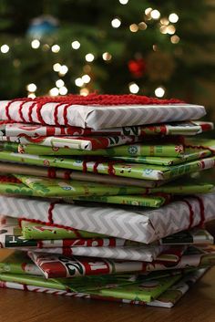 a stack of wrapped presents sitting on top of a table next to a christmas tree