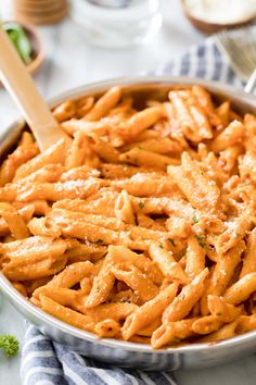 a pan filled with pasta and parsley on top of a white table cloth next to utensils