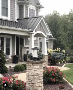 a house that has some flowers in the front yard and bushes on the side of it