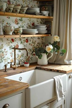 a kitchen with floral wallpaper and wooden shelves above the sink is filled with dishes