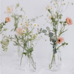 three clear vases filled with different types of flowers on a white tableclothed surface