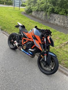 an orange and black motorcycle parked on the side of the road next to some grass