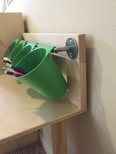 there is a green cup that has been placed on the shelf with several pencils in it