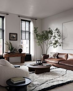 a living room with leather couches and tables in front of two large windows that look out onto the street