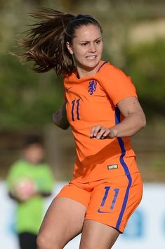 a female soccer player in an orange uniform kicking the ball with her hair blowing in the wind