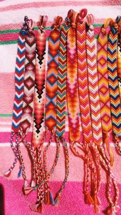 several bracelets are hanging on a pink and white blanket with tassels attached to them