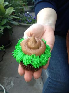 a hand holding a cupcake with green frosting and a brown hat on top