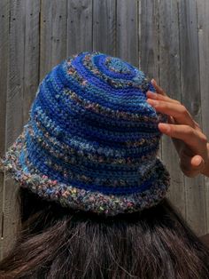 a woman wearing a crocheted blue hat with multicolored yarns on it