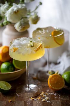 two margaritas sitting on top of a table next to oranges and limes