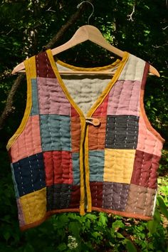 a colorful vest hanging from a tree in front of some trees and bushes with green leaves