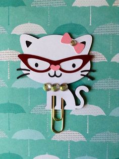 a white cat with glasses and a pink bow on it's head is holding an umbrella clip