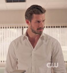 a man in a white shirt is looking at something on the table with his hands behind him