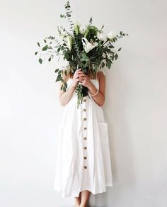 a woman in a white dress holding a bunch of flowers over her face with both hands