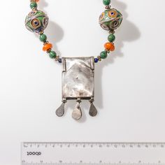 This 25" necklace features a green burnt orange and lapis-blue vintage enameled Berber Hirz pendant with a Star of David, strung together with large Berber enameled Moroccan beads of matching colors, African green jade beads, Vintage Berber Amber Resin beads and low-grade silver Yemenite wire spacers. Two Lapis Lazuli beads emphasizing the blue of Star of David delineate the pendant from the rest of the necklace. The Hirz pendant had three traditional decorative dangles, and is 85x40 mm long. Th Orange Amulet Pendant Jewelry, Bohemian Silver Enamel Necklaces, Silver Amulet Necklace With Colorful Beads, Artisan Green Necklaces With Dangling Beads, Artisan Green Necklace With Dangling Beads, Green Amulet Necklace For Festival, Orange Amulet-style Jewelry With Large Beads, Green Amulet-style Jewelry With Large Pendant, Green Pendant Necklace With Silver Beads