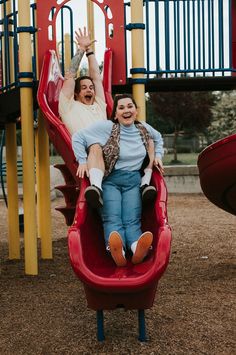 two women sitting on a red swing set at a playground with their arms in the air