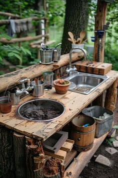 Rustic outdoor kitchen with wooden countertops, metal sink, and various utensils in a forest setting. Outdoor Kitchen With Pallets, Mud Room Kitchen Combo, Kitchen Combo Ideas, Outdoor Mud Kitchens For Kids, Kids Outdoor Kitchen, Easy Mud Kitchen, Diy Camp Kitchen, Mud Kitchen Diy, Pallet Mud Kitchen