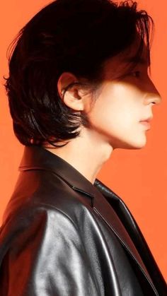 a woman with black hair wearing a leather jacket and looking off to the side in front of an orange background