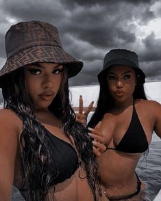 two beautiful women in bikinis standing next to each other near the ocean with dark clouds