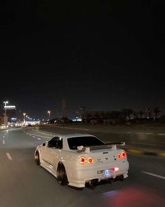 a white sports car driving down the road at night with city lights in the background