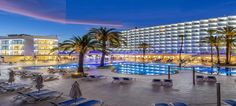 an outdoor swimming pool with lounge chairs and palm trees in front of it at night