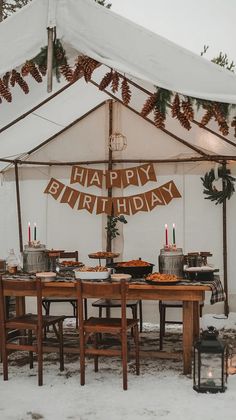 an outdoor birthday party setup up in the snow with candles and pine cones on it