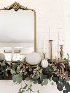 a mantel decorated with greenery, candles and white pumpkins on top of it