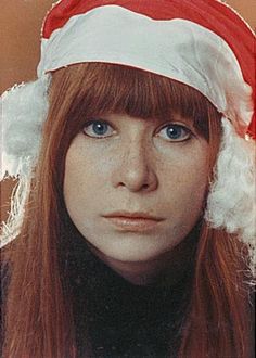 a woman with long red hair wearing a santa hat on top of her head and looking at the camera