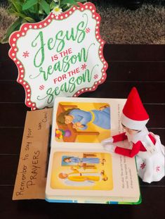 an elf is sitting on the floor next to some books and a sign that says jesus is the reason for the season