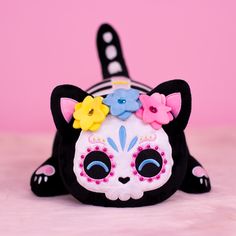 a black and white cat stuffed animal with flowers on it's head, laying down