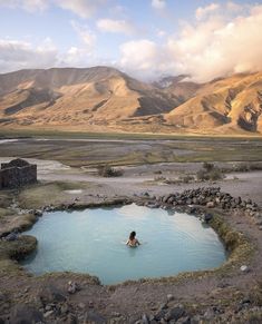 a man swimming in a blue pool surrounded by mountains