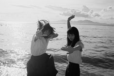 two young women standing on the beach with their arms in the air