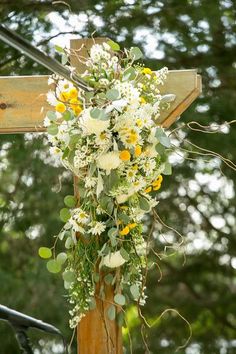 a cross with flowers and greenery hanging from it's sides in front of trees