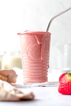 a pink smoothie in a plastic cup with a straw and strawberry on the side