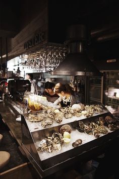 a woman standing behind a counter filled with oysters