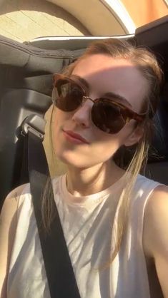 a woman sitting in the back seat of a car wearing sunglasses and a white tank top