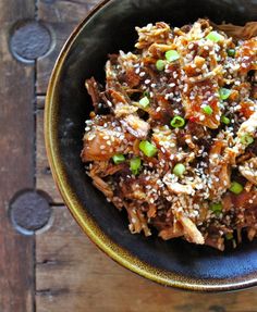 a black bowl filled with rice and meat on top of a wooden table next to chopsticks