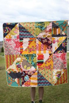 a person standing in the grass holding up a colorful quilt