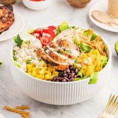 a white bowl filled with chicken, rice and beans next to other plates of food