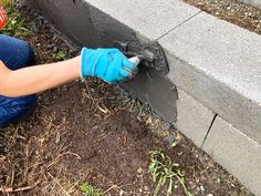 a person wearing blue gloves is working on the side of a building with dirt and grass