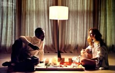 two people sitting on the floor in front of a lamp