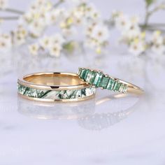 two gold wedding bands with green tourmaline and white flowers in the back ground