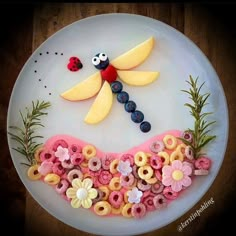 a white plate topped with fruit and flowers on top of a wooden table next to a lady bug