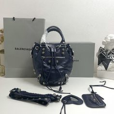 Balenciaga 's popular 'Le Cagole' series is a modern interpretation of its 'City' handbags - reshaped into a bucket bag design to inject a new soul into it. The large size adds two round top handles, combining classic and Modern trends are perfectly integrated. On the basis of retaining the original DNA of the motorcycle bag's flat rivets, delicate buckles and tassel zippers, it adds adjustable woven shoulder straps and a cute and playful heart-shaped mirror, which perfectly softens the neutral New Soul, Shaped Mirror, Motorcycle Bag, Lv Purse, Lv Shoes, Gucci Bamboo, Lv Belt, Lv Handbags, Lv Wallet