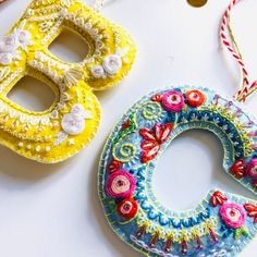 two colorful masks are sitting next to each other on a white surface, one is decorated with flowers and the other has buttons