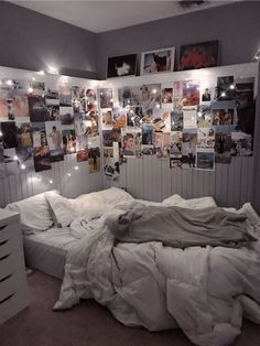 an unmade bed in a bedroom with pictures on the wall and lights above it