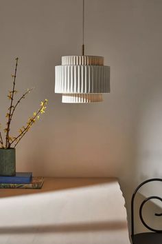 a lamp hanging over a bed next to a vase with yellow flowers on top of it