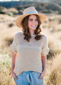 a woman wearing a straw hat standing in tall grass with her hands on her hips