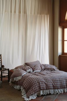 an unmade bed sitting next to a window in a room with white drapes