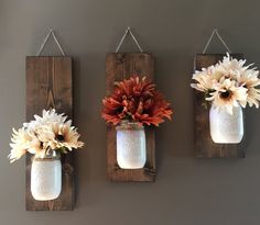 three mason jars with flowers hanging on the wall