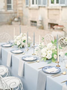 the table is set with blue and white plates, silverware, flowers and candles